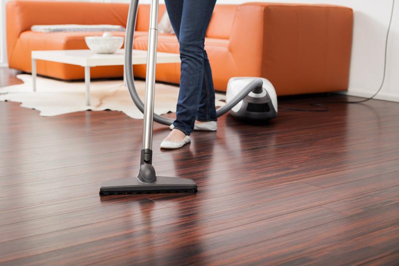 一个女人在用吸尘器清理硬木地板.