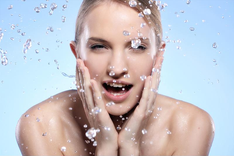 A woman washes her face by splashing water onto it.