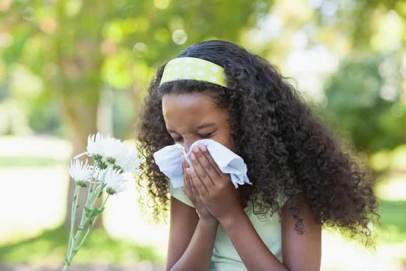 Girl sneezing into a tissue outside.